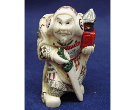 A Japanese carved ivory Okimono as a robed warrior holding a sword and carrying a lantern, 6cm high 