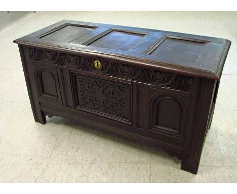 An 18th century carved oak kist of typical form, the hinged rectangular three panel lid over a carved frieze with central esc
