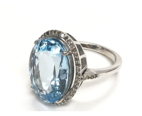 Oval dress ring in silver set with large oval blue topaz and a halo of R/C diamonds with a diamond set shoulders. Topaz 11.45