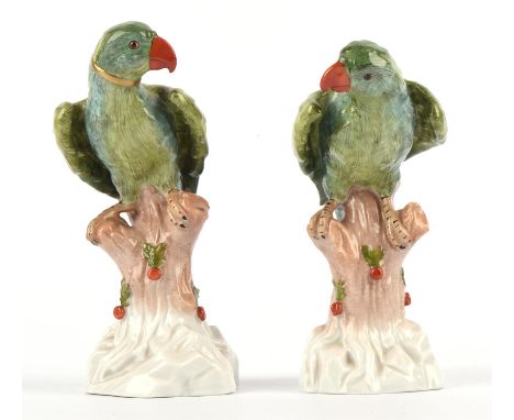 A pair of Dresden style porcelain green decorated parrots with orange beaks perched on tree trunk bases. 15cm high