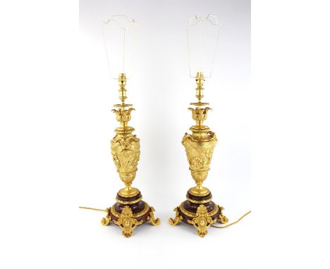 A pair of Louis XVI style gilt bronze and brass table lamps, the central urns cast with frolicking putti, on stepped red marb