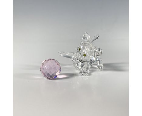 A clear faceted crystal figure of a playful small kitten, adorned with green eyes and accompanied by its pink toy ball. Swaro