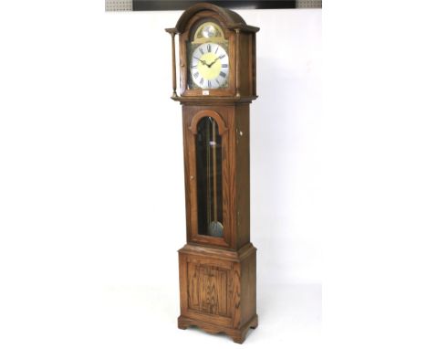 A contemporary longcase clock. The brass dial with Roman numerals, within a wooden case, raised on a bracket supports, with w