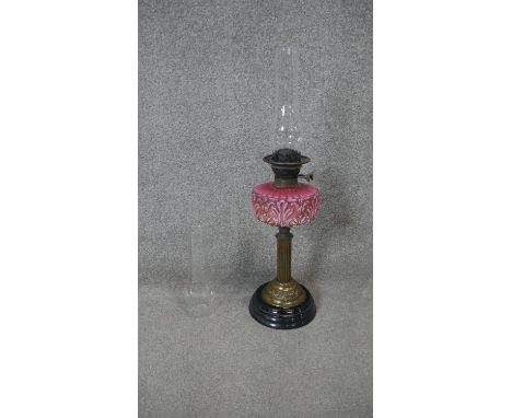 A late Victorian oil lamp, with an opaque pink glass foliate design relief well, the brass stand in the form of a column on a