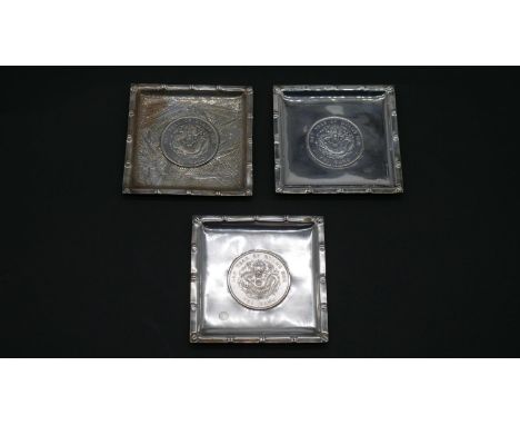 Three Chinese silver square pin trays, each with a Chinese dragon coin to the centre, one with an engraved bamboo design. Sta