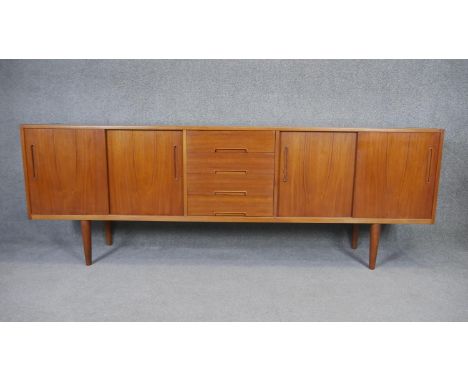 A 1970's vintage teak sideboard with a bank of central drawers flanked by sliding cupboard doors on circular section tapering