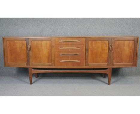 A vintage teak sideboard with central bank of drawers flanked by sliding cupboard doors on shaped stretchered supports. H.80 