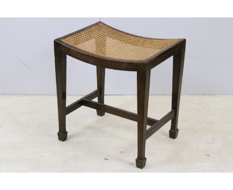 Arts and Crafts wooden stool with a shaped seat and canework finish, square tapering legs with arrow head feet, H 49cm