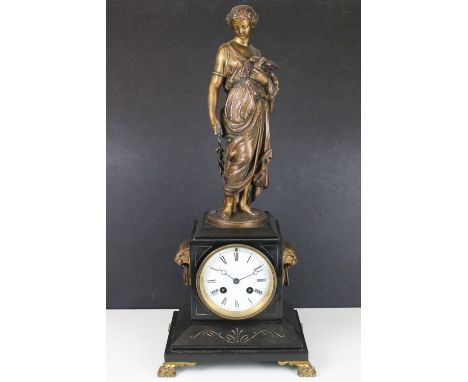 Cast metal lady with bird sculpture atop a black marble mantle clock base with ogre head side handles and lions paw feet