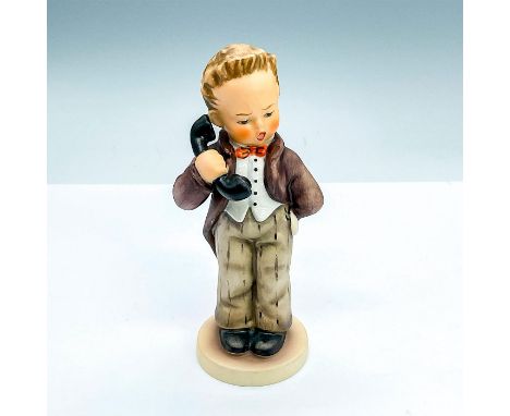 A ceramic figurine of a boy answering phone call. Brown jacket and pants; red bowtie; white shirt. Goebel backstamp. Issued: 