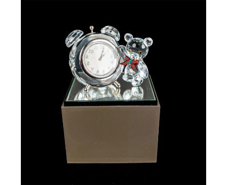 Mini teddy bear with green and red ribbon bow tie, standing next to a large alarm clock. This item has a base included which 