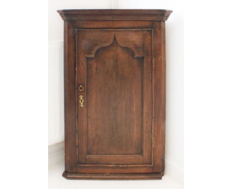 A late 18th century hanging oak corner cupboard: single panel arch-topped door opening to reveal green-painted shaped shelves