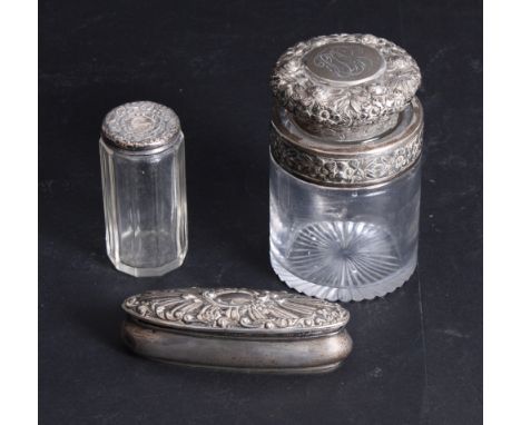 A cylindrical glass salts jar with repoussé decorated silver top, a silver topped toilet jar and an oval silver trinket box