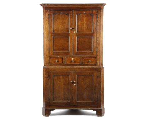 A George III oak standing corner cupboard, with a mahogany frieze, above a pair of arc d'arbelète panelled doors enclosing a 