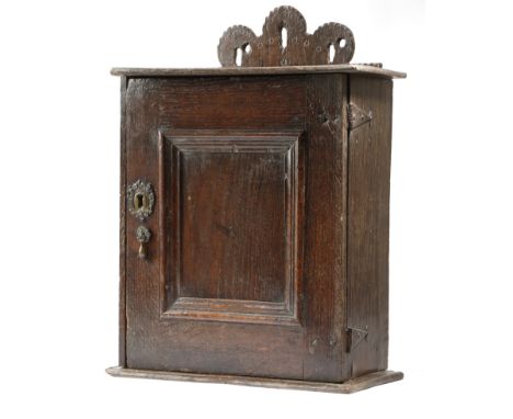 An oak hanging spice cupboard, the raised pierced back with carved and stamped decoration, above a moulded edge and a panelle