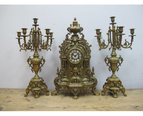 A XX Century German Rococo Style Brass Clock Garniture, the clock with enamel Roman numerals, the case with urn surmount and 