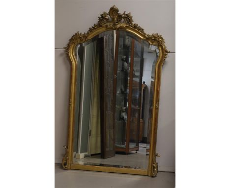 A faceted mirror in gilt ornamental frame with volutes and garland crowning, 19th century, h 136 x w 87 cm (mirror of later d