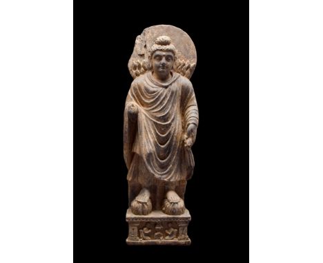 Ca. AD 100-200.A schist stone carving of a standing Buddha performing Twin Miracles. The figure stands upright, radiating an 