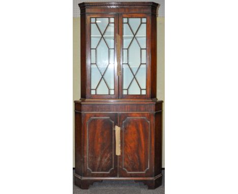 A 20th Century mahogany corner cupboard having a twin astragal glazed doors revealing a shelved interior above a twin door cu