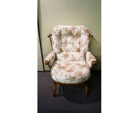 An Ercol style wide armchair having a spindle backrest, shaped arms and raised on shaped legs, all with chintz upholstered cu