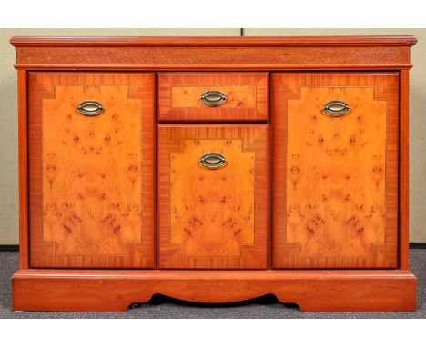 A reproduction yew wood sideboard having central drawer above cupboard flanked by cupboards to either side, all raised on sha