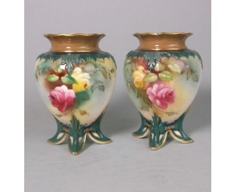 A pair of Royal Worcester porcelain vases: of egg shaped form with four peg feet, the shoulders moulded with foliage, painted