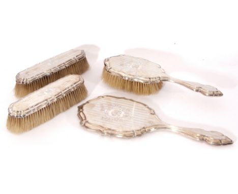 George V silver four-piece dressing table set comprising a hand mirror and three various brushes, the silver backs decorated 
