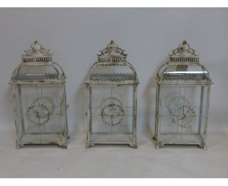 A set of three contemporary storm lanterns, distressed painted and with floral decoration, raised on bracket feet, H.59 W.28 