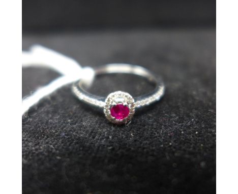 A boxed 18ct white gold ruby and brilliant-cut diamond ring, centrally set with a faceted oval-shaped ruby framed by diamonds