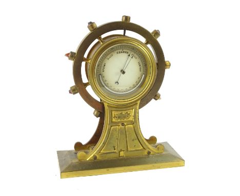 An early 20thC brass cased barometer, the 13cm diameter dial in a ship's wheel case on rectangular base, 33cm H (AF).