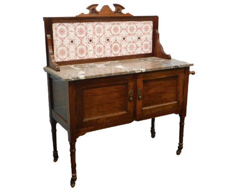 An Edwardian walnut wash stand, the raised back with pink patterned tiles, the base with a marble top above two panelled door