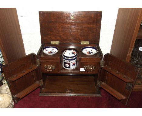 An Edwardian oak smoker's cabinet, the hinged rectangular lid opening to reveal a central shelf flanked by two recesses, abov