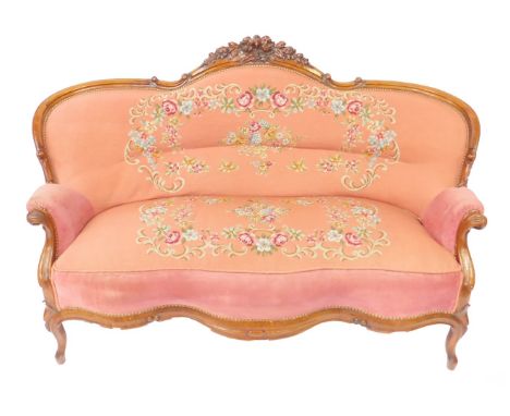 A Victorian walnut balloon back sofa, with foliate carved crest rail, floral wool work overstuffed seat and back, on a pink g