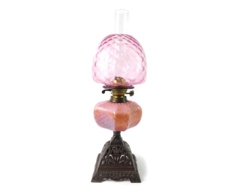 An early 20thC cast iron oil lamp, with a pink honeycomb opaline glass reservoir, with chimney and cranberry glass shade, 57c