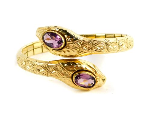 An early 20thC Continental gold plated bangle, formed as a double headed serpent inset with oval cut purple paste to the head