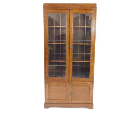 An early 20thC oak cupboard bookcase, with a pair of lead glazed doors opening to reveal three shelves, over cupboard doors, 