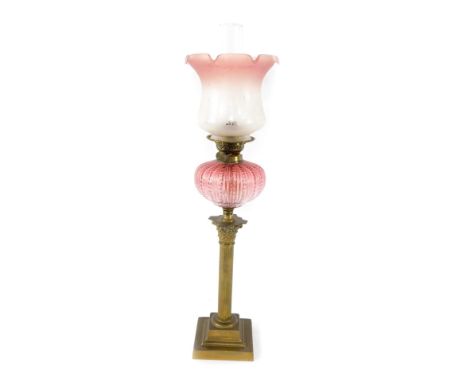An early 20thC brass Corinthian column oil lamp, with a fluted cranberry glass reservoir, with chimney, and floral etched cle