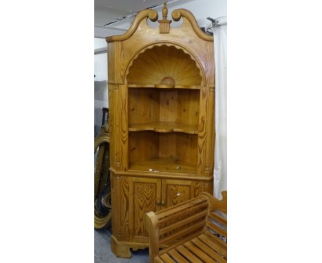 A large polished pine open corner display cabinet, with swan-neck pediment and starburst recessed alcove, with cupboard doors