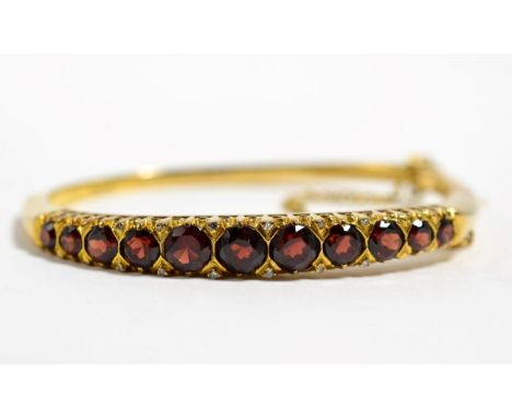 A 9 carat gold garnet bangle, graduated round cut garnets with single-cut diamond accents, 22.5g  