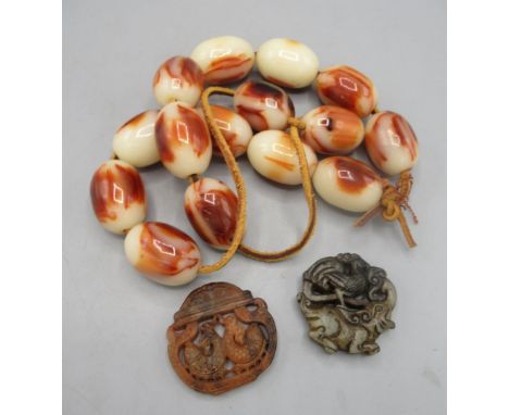 Red jade pendant with two carp in bowl, a green jade pendant with elephant and peacock design, and a row of cream and brown b