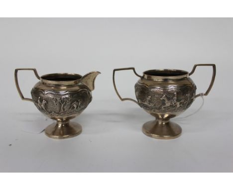 AN INDIAN WHITE METAL MILK JUG with chased and engraved decoration of a hunting scene with looped handle and standing on circ
