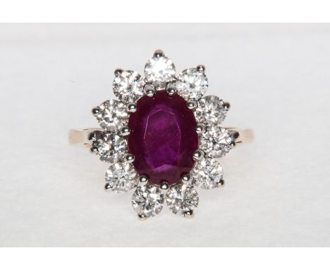 A ruby and diamond oval cluster ring, the oval mixed cut ruby surrounded by diamonds (11) brilliant cut stones and claw set i