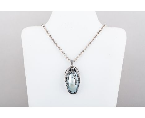 An oval mother of pearl shell pendant with black onyx back in a white metal setting with applied leaf and floral mounts 60mm 