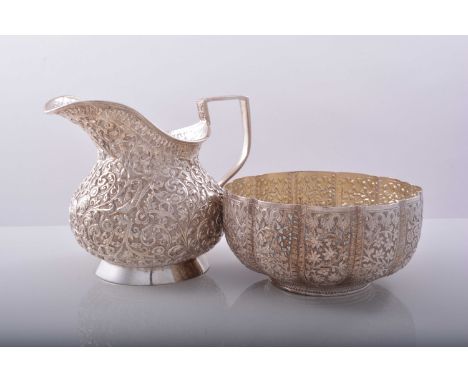 An Indian white metal pear shape jug, probably late 19th Century, squat form, cast and chased decoration of birds amongst scr