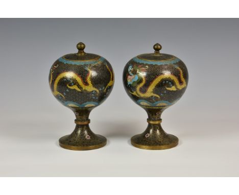 A pair of Chinese cloisonné pedestal jars and covers black ground, depicting dragons chasing flaming pearl, 8in. (20.4cm.) hi