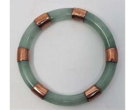 A jade slave bangle, c.1920's, with yellow metal mounts, external diameter 94mm.
