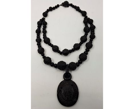 A Victorian jet mourning pendant and necklace, the oval pendant carved monogram within wreath to front and with inset waterco