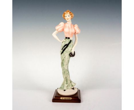 Features a lady standing wearing a pink blouse with green and white skirt. Armani Florence golden plate on wooden base. Giuse