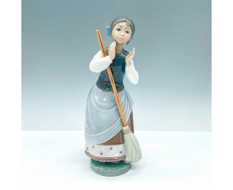 Elegant, glazed figurine of girl clapping hands together with a broom in her arms. Crafted in subtle hues of blue and brown. 