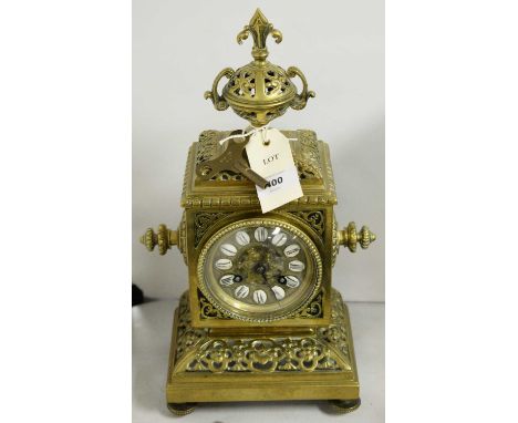 An ornate brass mantel clock, the brass dial with white ceramic hour markers bearing Roman numerals in black, within twin han